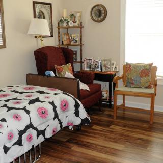 Cozy bedroom with a floral-patterned bedspread, armchair, and decorative shelving.