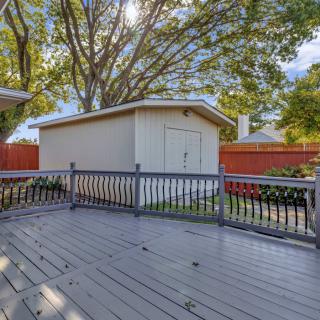A backyard featuring a wooden deck and a small shed with tall trees in the background.