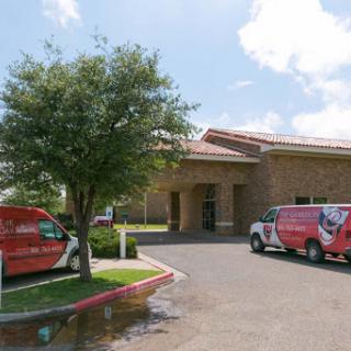 A view of a commercial building with parked vehicles and a tree in front.