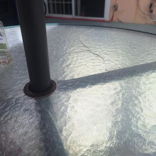 A close-up view of a glass table with reflections and shadows created by an adjacent pole.