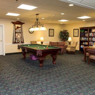 A cozy game room featuring a billiard table and a quiet seating area with bookshelves.