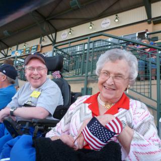 Elderly woman and man at a stadium, smiling and holding an American flag.
