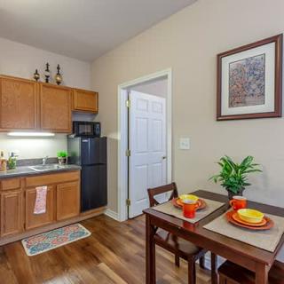 A cozy kitchenette with a small dining area, featuring a fridge, microwave, and wooden cabinets.