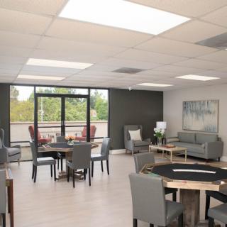 A modern lounge area with tables, chairs, and large windows offering a view of the outdoors.