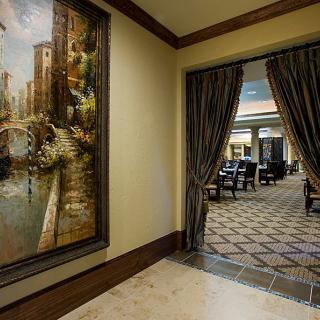 A hallway with a large painting and curtains leading to a furnished lobby area.
