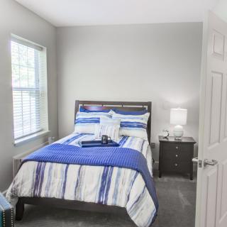A cozy bedroom with a neatly made bed and a nightstand under soft lighting.