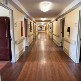 A long, well-lit hallway with wooden floors and doors on either side.