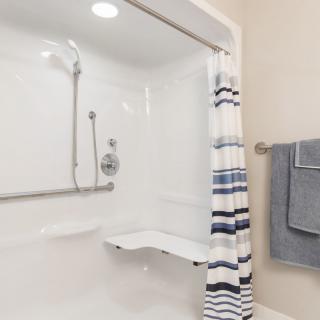 A modern bathroom featuring a shower with a striped curtain, grab bar, and folding seat.
