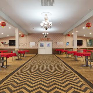 A spacious dining area featuring red tablecloths and a stylish chandelier, illuminated by soft overhead lighting.