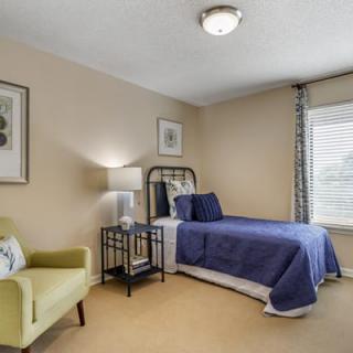 A cozy bedroom with a single bed adorned in blue bedding, an armchair, and large windows letting in natural light.