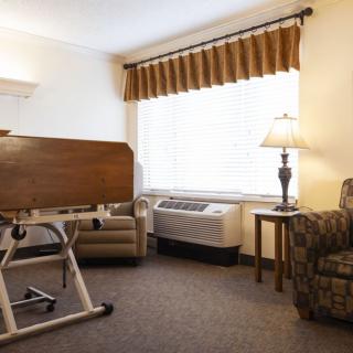 A hospital room with a bed, chair, and lamp by the window.
