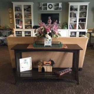 A cozy living room featuring a console table with decorative items and flowers, positioned in front of bookshelves.
