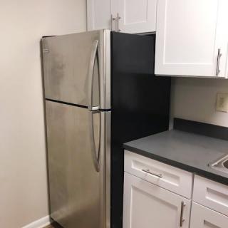 A stainless steel refrigerator in a modern kitchen with white cabinets.