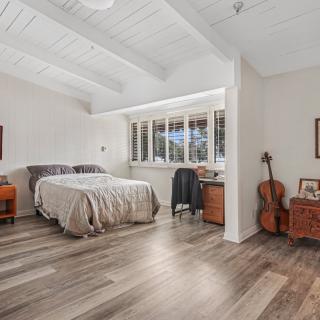 A cozy bedroom with wood flooring, featuring a bed, guitar, and natural light streaming through the window.