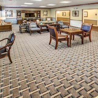 A spacious lobby with seating arrangements featuring wooden tables and chairs on a patterned carpet.