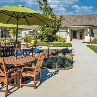 A sunny outdoor patio with tables and umbrellas set in a landscaped garden.