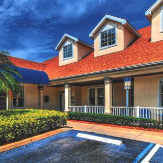 A residential house with a red roof and manicured landscaping under a blue sky.