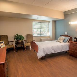 A clean and minimalist hospital room with a bed, chairs, and a window.
