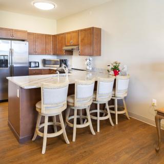 A modern kitchen with wooden cabinets and bar stools along a central countertop.