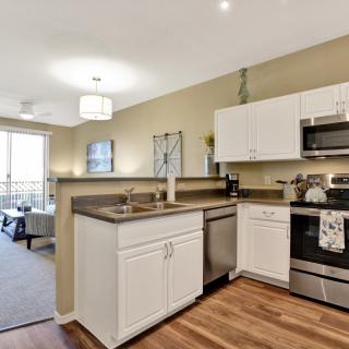 A modern kitchen in an open floor plan apartment with stainless steel appliances and wooden flooring.