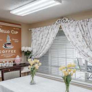 A cozy dining area with floral curtains, vases of yellow tulips on the table, and a vintage coffee poster on the wall.