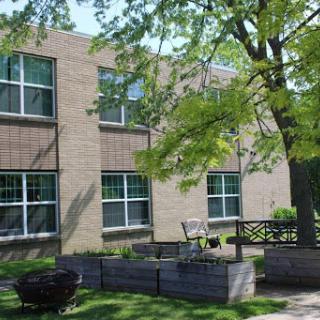 A view of a brick building surrounded by lush greenery and outdoor seating.