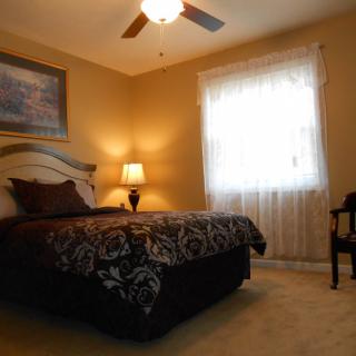 A cozy bedroom with a bed, lamp, and window featuring sheer curtains.
