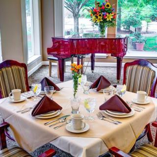 An elegantly set dining table with a grand piano in the background, overlooking a scenic window view.