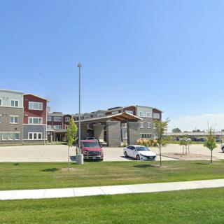 A modern apartment complex with landscaped surroundings and a parking area on a clear day.