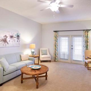 A cozy living room with a sofa, coffee table, and armchairs, featuring a ceiling fan and French doors.