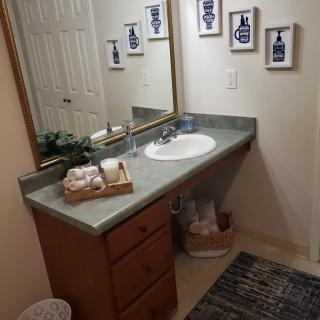 A neatly organized bathroom featuring a sink with a countertop, wall art, and a decorative basket.