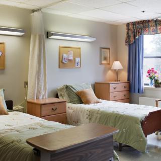 A clean and well-organized hospital room with two beds, bedside tables, and a window providing natural light.