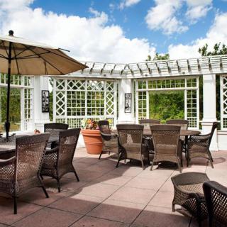 A sunny outdoor patio with wicker chairs and tables under a pergola.