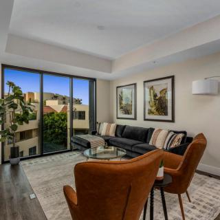 A modern living room with a black sofa, brown chairs, and large windows offering a view of the outdoors.