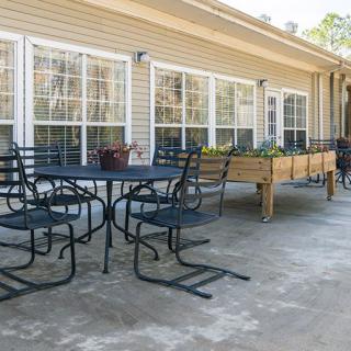 A patio with metal chairs and tables, adjacent to a building with large windows and planters.
