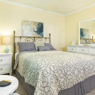 A cozy bedroom with a well-decorated bed, nightstand, and dresser featuring a mirror.
