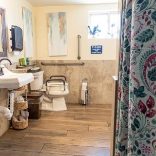 An accessible bathroom featuring a toilet with grab bars, a sink, and a shower with a floral curtain.