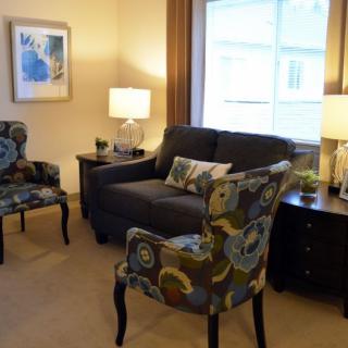 A cozy living room with a dark sofa, patterned armchairs, and warm lighting.