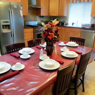 A kitchen with a dining table set for a meal, featuring a floral centerpiece and neatly arranged tableware.