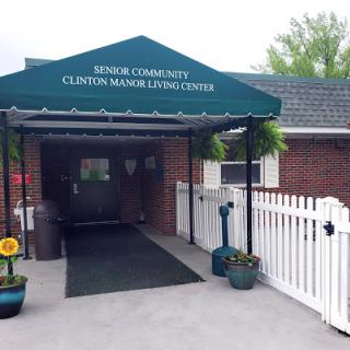 The entrance to the Clinton Community Senior Living Center, featuring a welcoming green awning and landscaped surroundings.