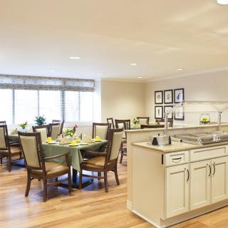 A modern dining room with a kitchen area featuring elegant tables and chairs on wood flooring.