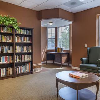 A cozy reading area in a library with bookshelves, an armchair, and a window letting in natural light.