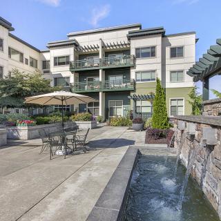 A modern apartment building with an outdoor area featuring a fountain and patio furniture.