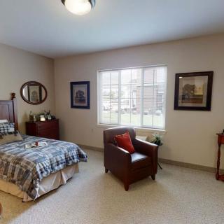 A cozy bedroom with a bed, chair, and window letting in natural light.