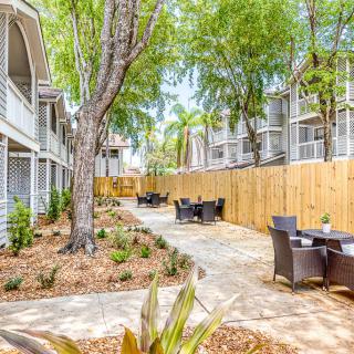 A serene outdoor seating area with tables and chairs surrounded by apartment buildings, trees, and a wooden fence.