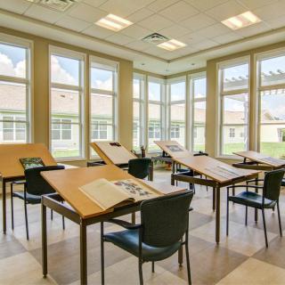 An empty classroom with drafting tables and large windows allowing natural light inside.