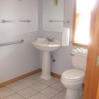 A small bathroom with a pedestal sink, toilet, mirror, and towel rack.
