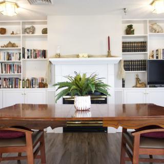 A modern dining room with a large wooden table, surrounded by chairs and flanked by bookshelves filled with books and decorations.