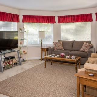 A cozy living room with a sofa, television, coffee table, and large windows adorned with red curtains.