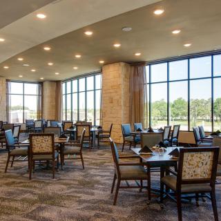 A spacious dining area with large windows, featuring neatly arranged tables and chairs.